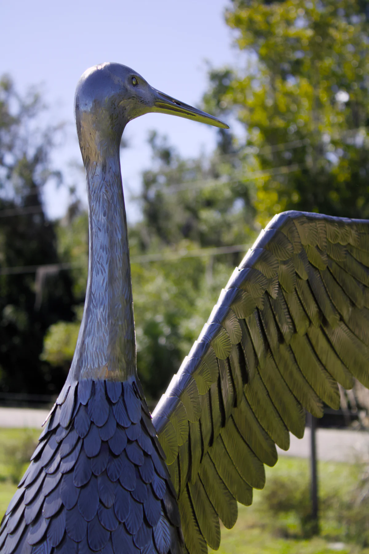 Side view of the crane's sculpted head and neck against the garden surroundings.