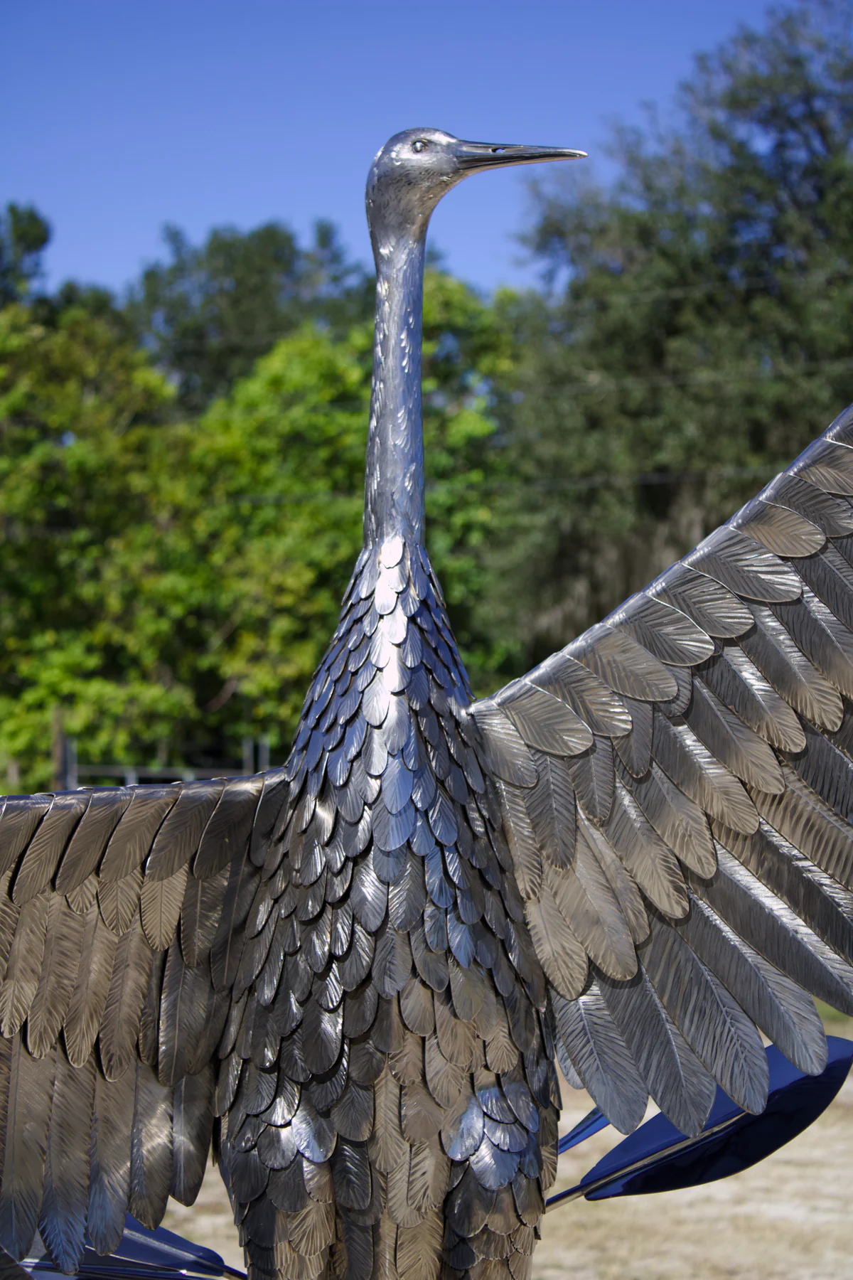Front view of the crane's layered metal feathers across its body and outstretched wing.